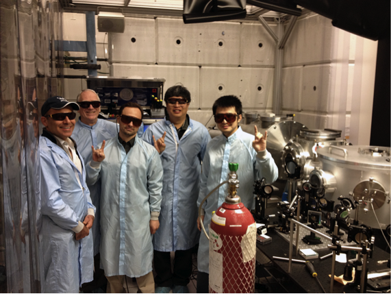 The petawatt laser-plasma acceleration team next to their apparatus in the Texas Petawatt Laser target bay.  L to R:  Neil Fazel, Dr. Watson Henderson, Dr. Rafal Zgadzaj, Dr. Xiaoming Wang and Zhengyan Li. The hand symbol signifies “2 GeV”.